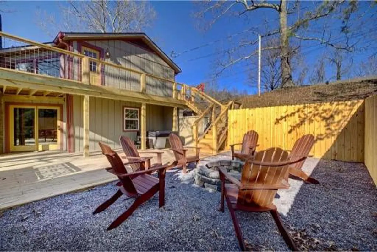 This image features a cozy exterior space with a fire pit surrounded by Adirondack chairs, a large wooden deck, and an inviting staircase. The space is clearly designed for social gatherings and outdoor relaxation, ideal for family cookouts or evenings spent together under the stars.