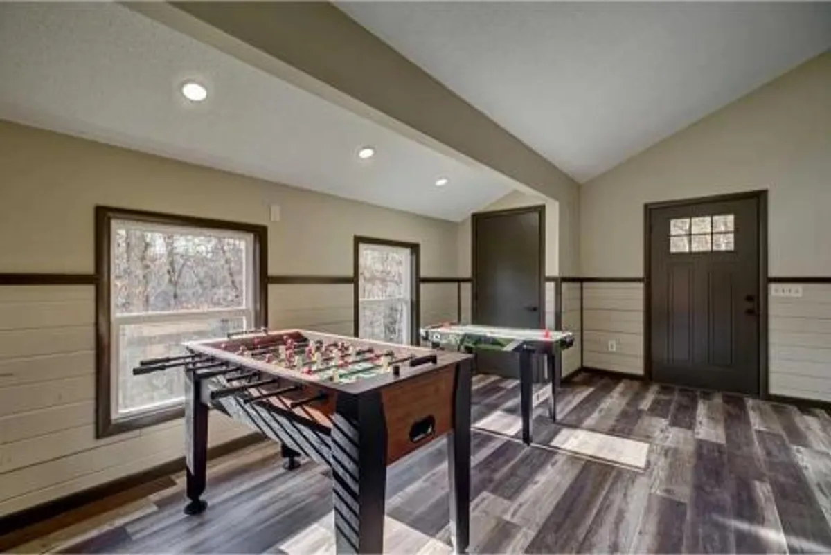 A bright, cheerful game room featuring a foosball table and a game table, with large windows that bring in natural light and views of the outdoors. The setup is playful and social, ideal for group game nights and friendly competition among guests.