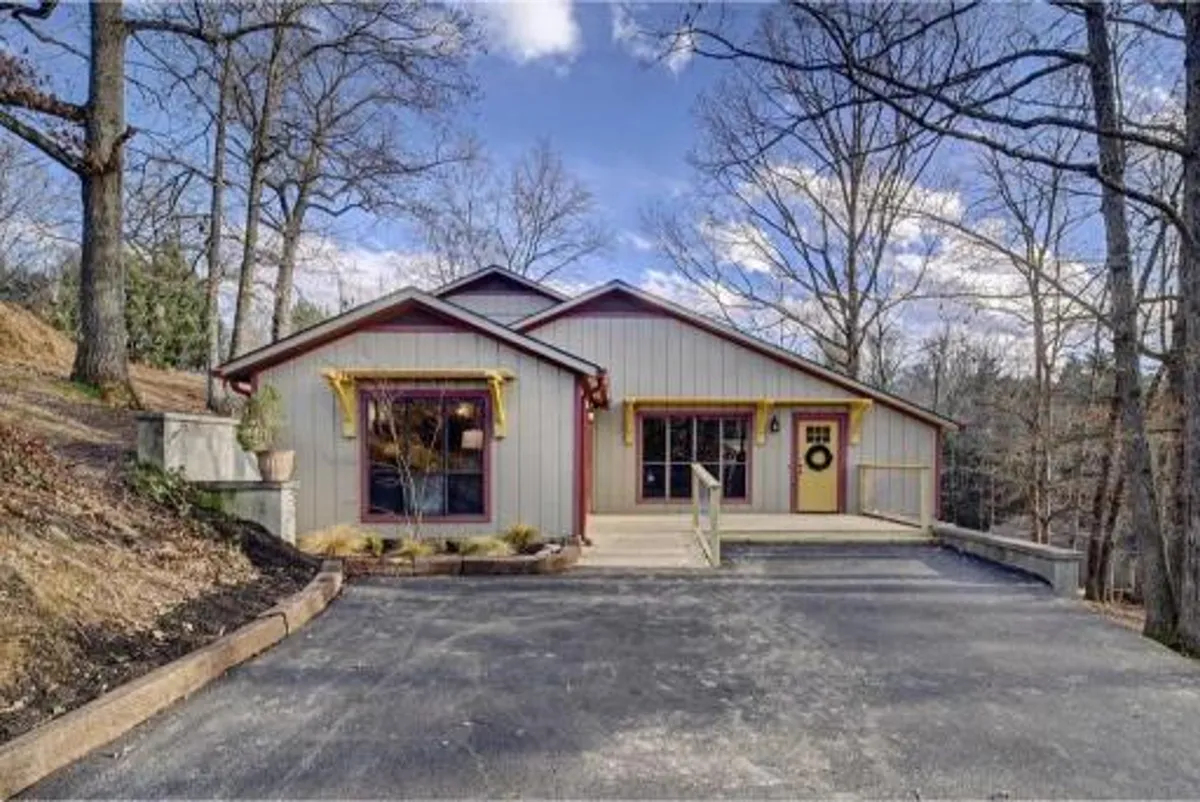 The image showcases the inviting front entrance of a newly remodeled cabin, adorned with a cheerful round wreath and decorative yellow trim. Large windows hint at the natural light and mountain views inside, while a spacious porch suggests a perfect spot for relaxation or family gatherings. The scene is bright and welcoming, embodying the spirit of a Smoky Mountain retreat.