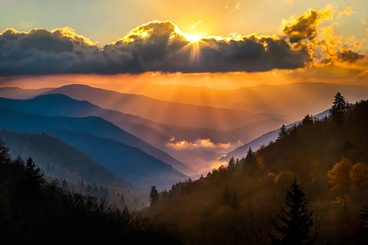 A breathtaking view of sunset over rolling mountain ridges, with clouds and fog filling the valleys below. The colors and atmosphere evoke the serene beauty of the Great Smoky Mountains, ideal for hiking, photography, and nature appreciation.