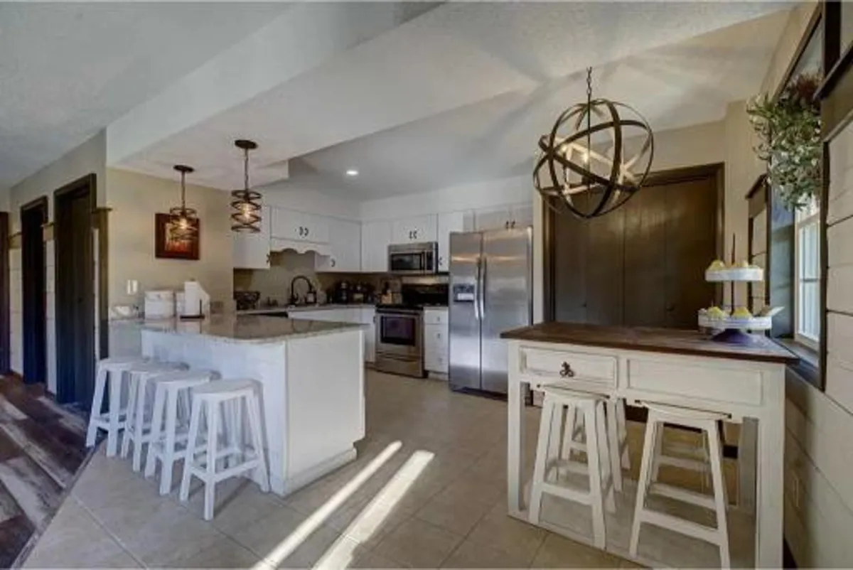 A spacious kitchen with a central island featuring seating, pendant lights overhead, high-end appliances, and warm decorative touches on the countertop. The layout is open and inviting, designed for group cooking and casual conversation.