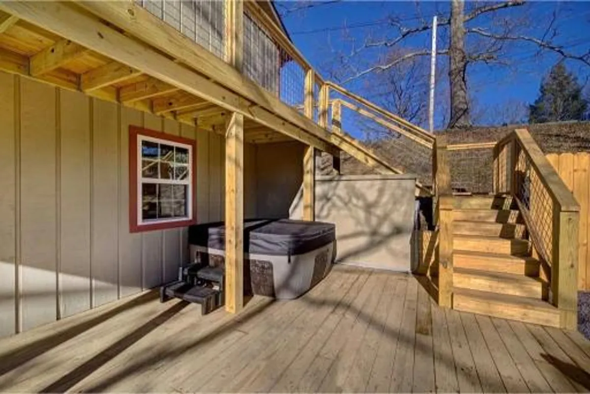 A spacious wooden deck equipped with a bubbling hot tub, surrounded by outdoor seating and a staircase leading down. The area is bathed in natural light, evoking a sense of relaxation and enjoyment of the outdoors.