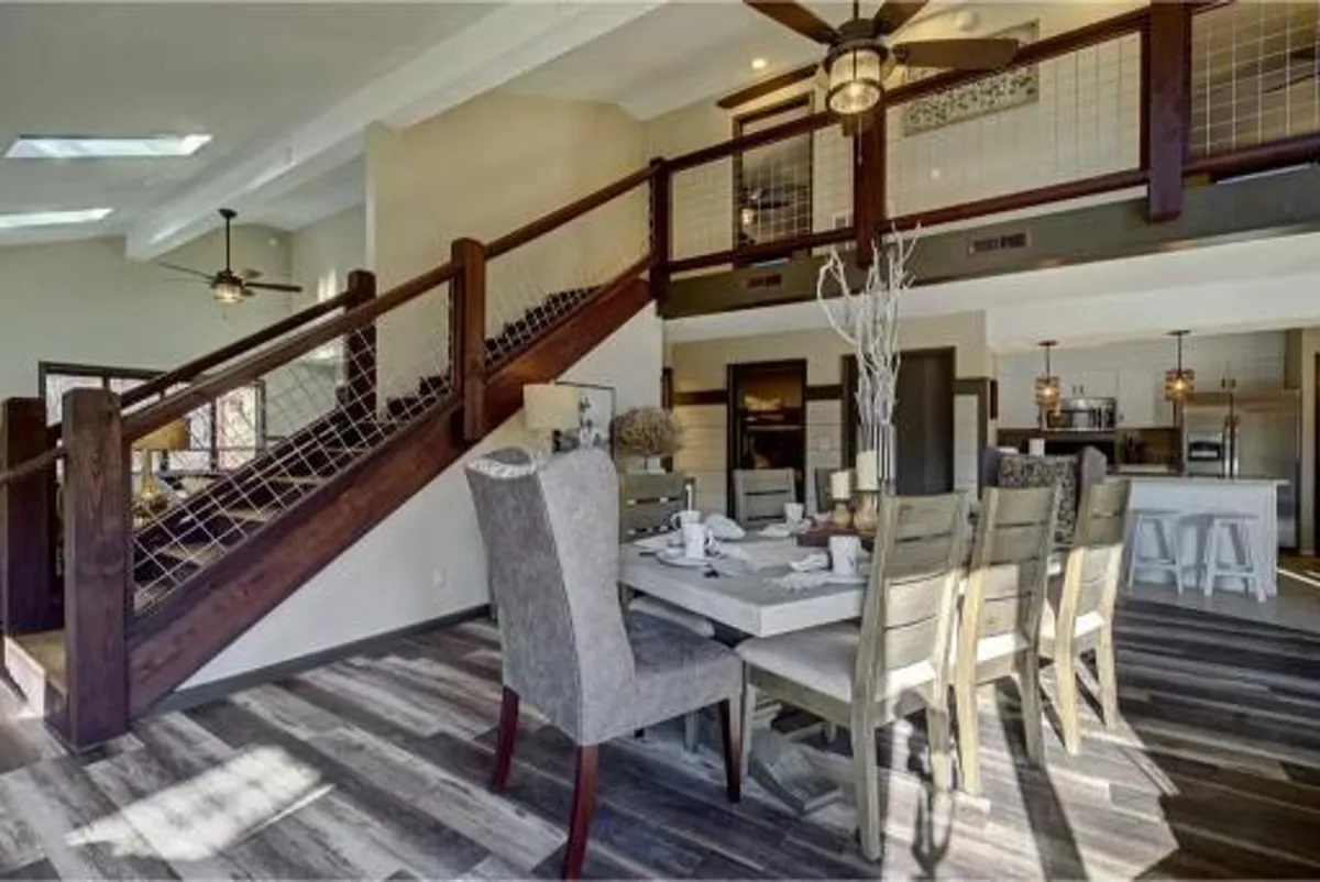 An elegant dining area centered around a large table, with sophisticated light fixtures above and a staircase in the background. The atmosphere is inviting, ideal for family dinners, celebrations, or game nights.
