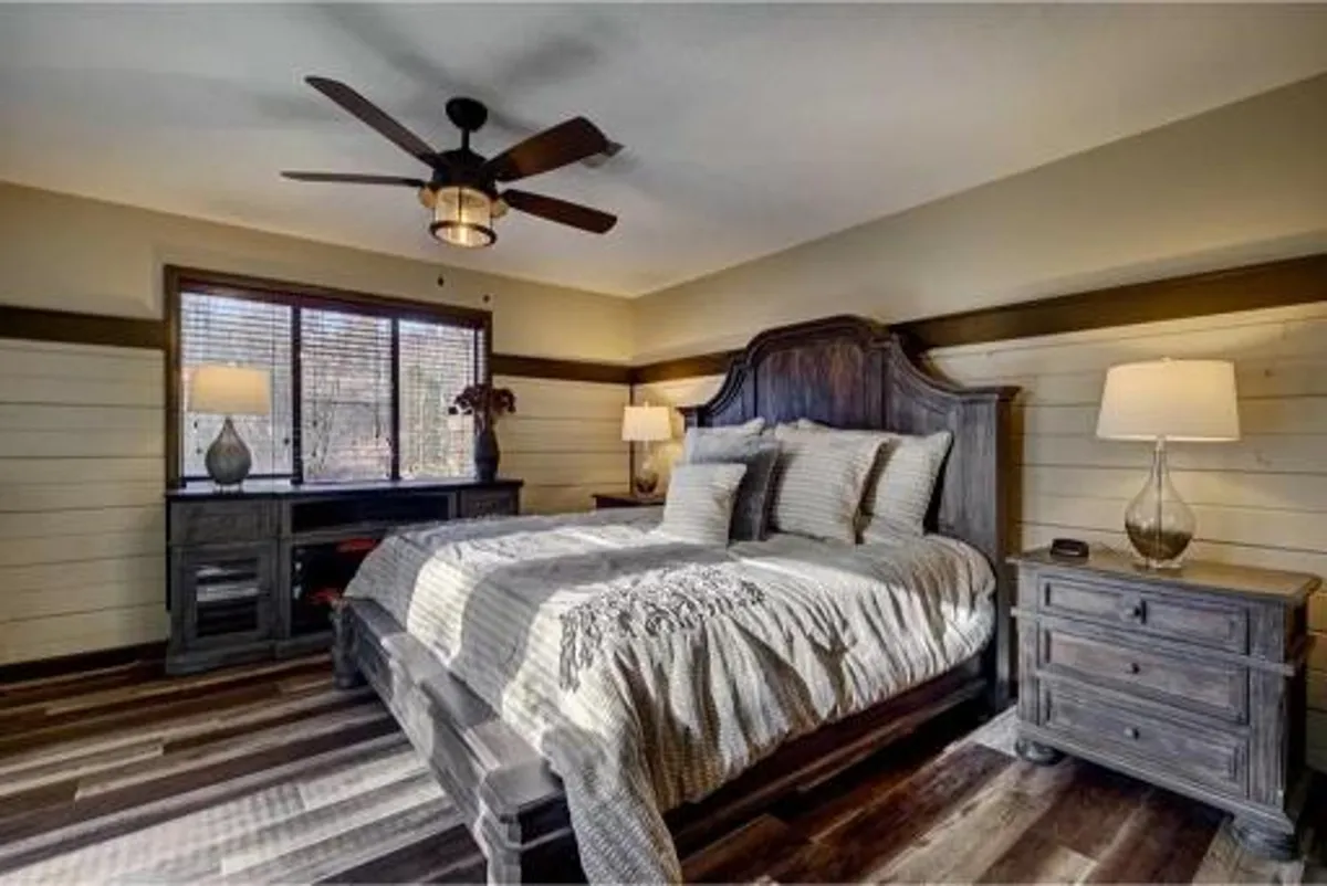 This image features a welcoming bedroom with a comfortable bed, nightstands, a window, and a dresser. Soft natural light filters through the blinds, creating a tranquil and peaceful ambiance ideal for restful sleep.