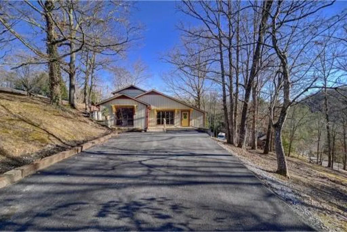 An inviting view of the house facade, framed by surrounding trees and a welcoming driveway. The front porch beckons for outdoor gatherings or quiet moments, evoking a sense of arrival and seclusion.
